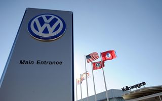 Stabilimento automobilistico Volkswagen con catena di montaggio e operai al lavoro, sfondo con logo aziendale